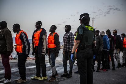 Un grupo de inmigrantes rescatados espera para ser identificado bajo la vigilancia de Guardia Civil, el cuerpo de seguridad responsable. Después serán atendidos por personal de Cruz Roja, encargados de la asistencia tras desembarco. Por último, una vez realizada la primera atención, pasarán a manos de Policía Nacional para ser identificados.