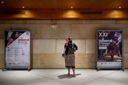 Una mujer con mascarilla en el Teatro Central de Sevilla, junto a dos carteles de la muestra. En esta edición, la obra ha sido creada por la artista Lita Cabellut.