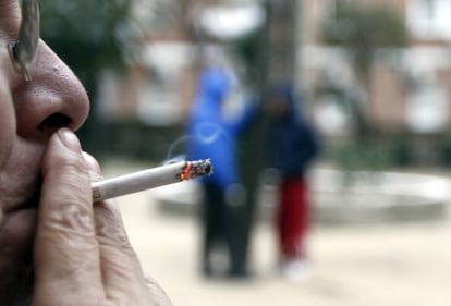 A woman smokes a cigarette in a park.