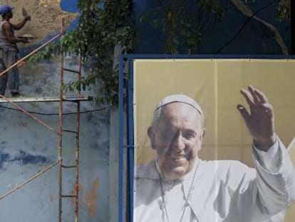 Um operário conserta um muro junto a um cartaz do Papa.