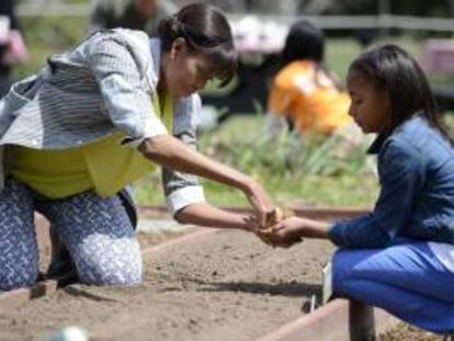 La primera dama estadounidense, Michelle Obama (i) ayuda a Ariana Docanto (d), una estudiante de quinto curso en la escuela de  Arthur D. Healey, a plantar semillas durante la quinta edición de cultivo de la Casa Blanca celebrada en el jardín sur de la residencia presidencial en Washington, Estados Unidos.