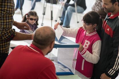 Una niña introduce el voto de su padre en una mesa electoral.