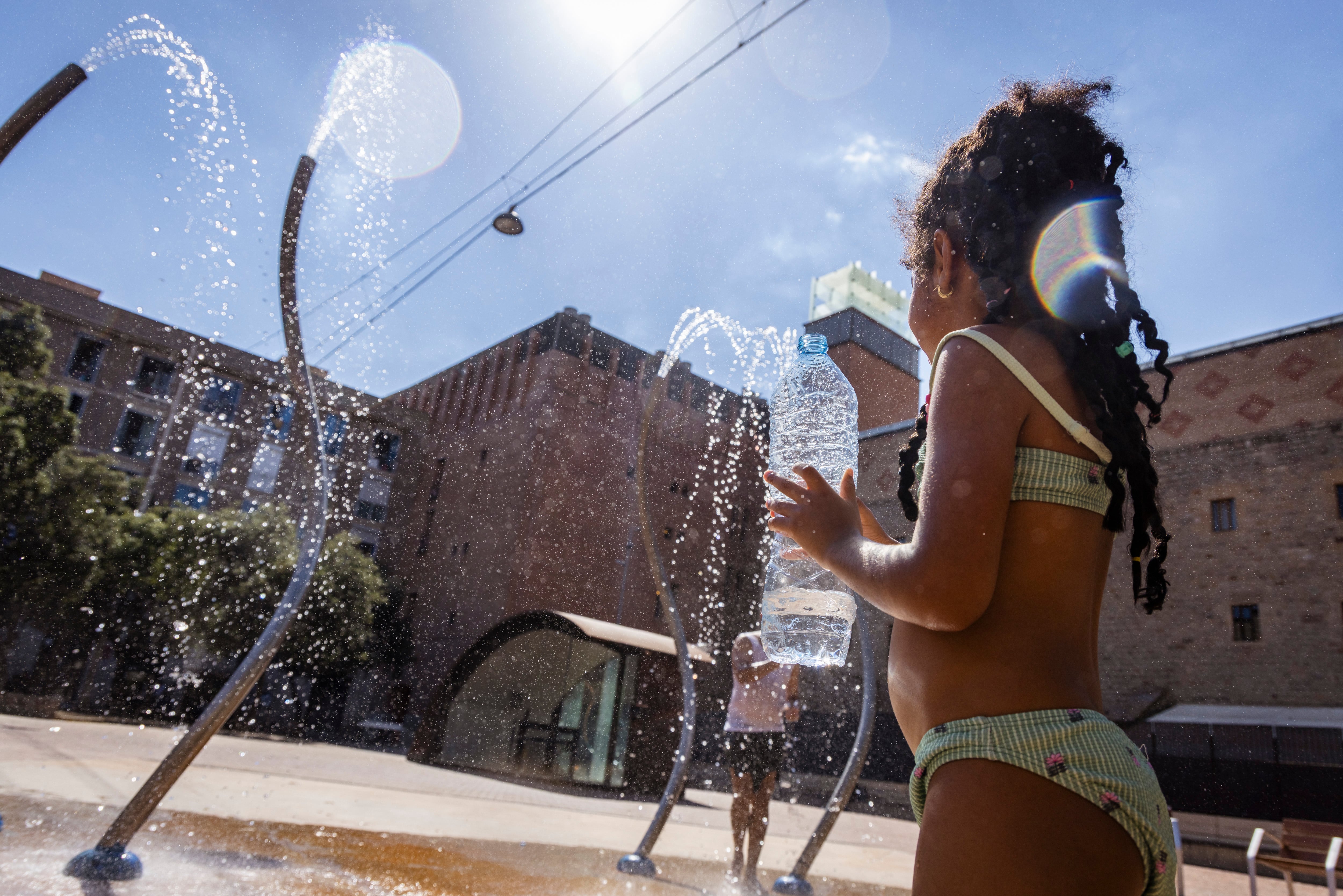 Una niña se refresca en la plaza de Les Caramelles del barrio del Raval de Barcelona, durante la segunda ola de calor de este verano.