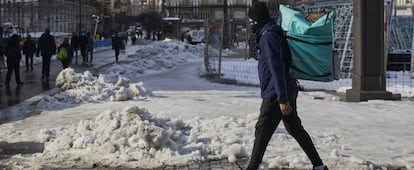 Un empleado de Deliveroo camina con su mochila de reparto por la Puerta del Sol nevada tras restablecer parcialmente el servicio, en Madrid, (España).