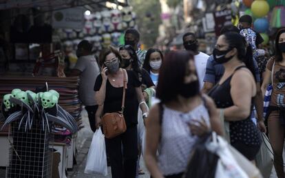 Pessoas caminham usando máscaras de proteção em uma rua de comércio popular no Rio de Janeiro.