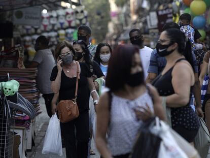 Pessoas caminham usando máscaras de proteção em uma rua de comércio popular no Rio de Janeiro.