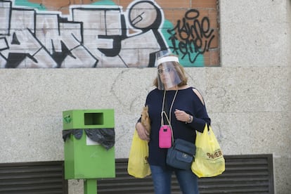 Una mujer protegida con una pantalla de plástico camina con bolsa de la compra, esta mañana, en Manzanares el Real.