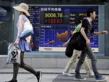 Varios viandantes pasan delante de una pantalla que muestra varios valores bursátiles en Tokio (Japón). EFE/Archivo