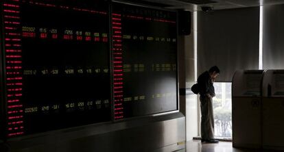 Un inversor mira hacia la calle ante un monitor de cotizaciones en Pek&iacute;n, China. 