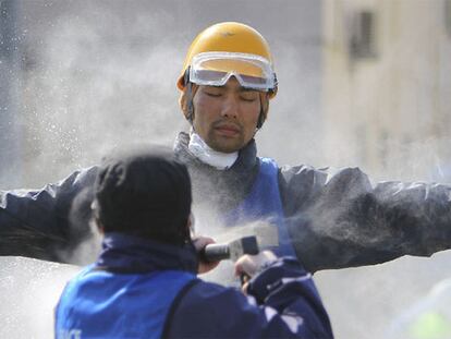 Un operario quita con agua el polvo de un voluntario en las tareas de reconstrucción de las zonas devastadas por el tsunami.
