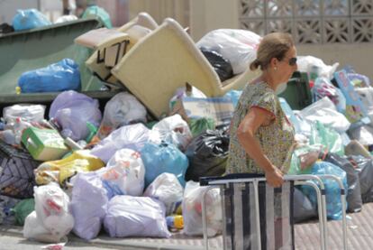 Una mujer pasa camino de la playa junto a un montón de basura amontonado como consecuencia de la huelga en Barbate.