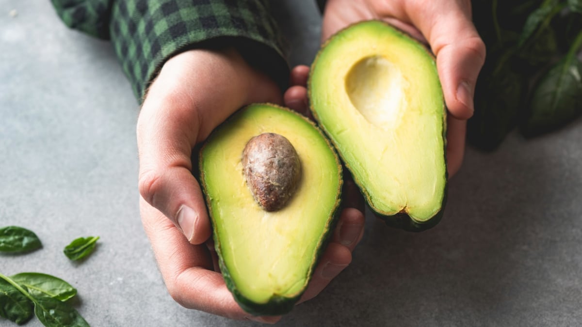 Un aguacate partido por la mitad, sostenido por unas manos.