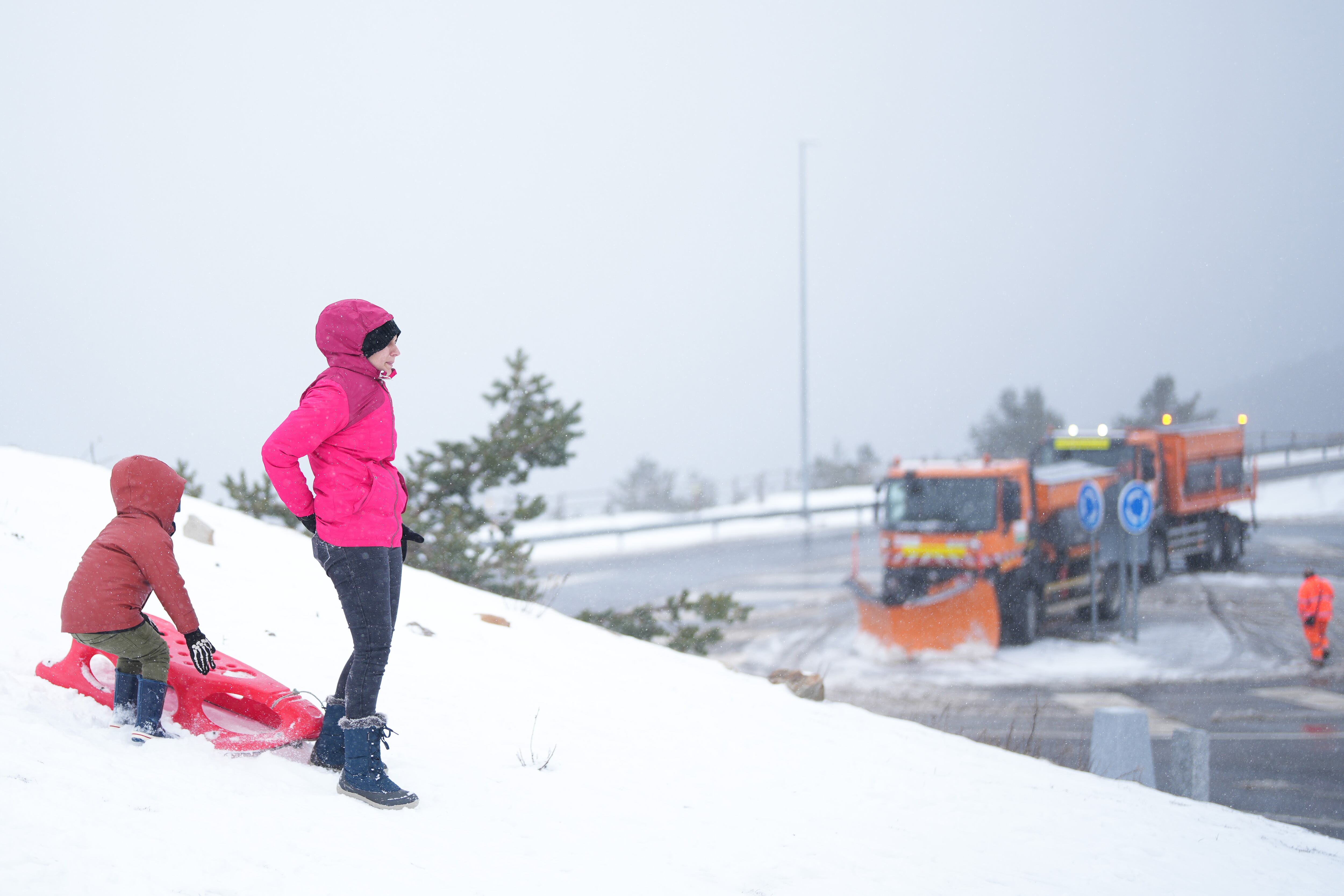 Una máquina quitanieves circula este martes junto a una mujer y un niño en el Puerto de Navacerrada, en la primera nevada del año en dicha estación invernal. 