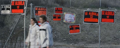 Una pareja pasea ante una valla con carteles de pisos en venta y en alquiler en Madrid.