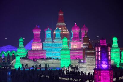 Cientos de visitantes pasean de noche por un edificio iluminado.