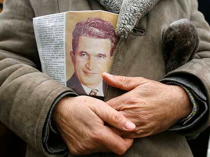 Un hombre sostiene un periódico con la imagen del ejecutado dictador Nicolae Ceausescu ante su tumba, en Bucarest.