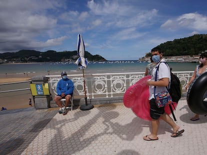 Unos jóvenes con mascarilla pasan ante el punto de control de aforo de la playa de La Concha en San Sebastián.