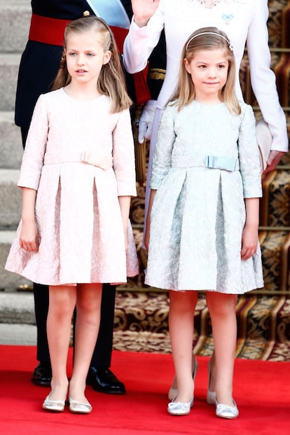 La princesa Leonor y la infanta Sofía también han sido protagonistas de los actos de proclamación. Para la ocasión, las niñas han llevado el mismo vestido. El diseño, de manga francesa y lazo zapatero doble en la cintura están elaborados en seda natural brocada con mezcla de algodón. Leonor lo ha elegido en rosa maquillaje y su hermana Sofía en azul verdoso.