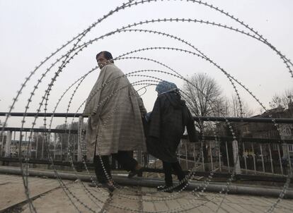 Dos personas caminan junto a una barricada de alambres en Srinagar, Cachemira, India. Cachemira sufre la segunda jornada de cierres, restricciones y toque de queda con motivo del primer aniversario de la muerte de Mohamed Afzal Guru, ahorcado por participar en un ataque al Parlamento indio en 2001.