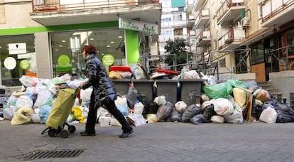 Una mujer pasa ante un grupo de contenedores rodeados de bolsas de basura, en una calle de Alcorc&oacute;n.