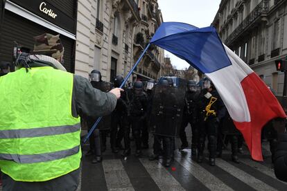 Un 'chaleco amarillo' ondea una bandera francesa junto a los policías antidisturbios este sábado en el centro de París.