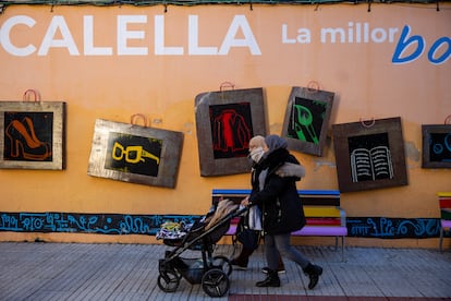 Dos mujeres con velo y un carrito de bebé pasean por delante de un mural que promueve el comercio de Calella.
