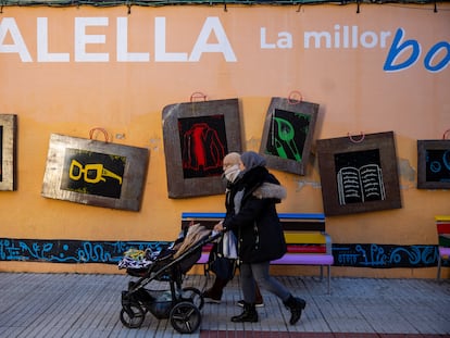 Dos mujeres con velo y un carrito de bebé pasean por delante de un mural que promueve el comercio de Calella.