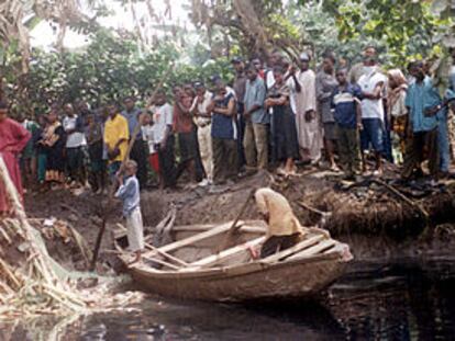 Vecinos de Lagos observan cómo dos voluntarios tratan de recuperar un cuerpo del canal donde murió ahogado.