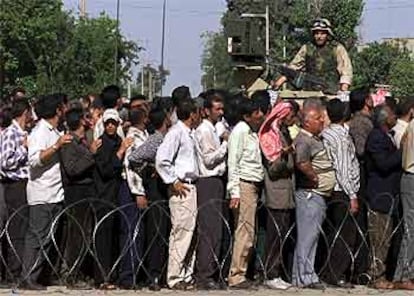 Empleados de una petrolera de Kirkuk guardan fila para el cobro del salario bajo la vigilancia de un soldado.