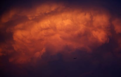 Un avión vuela por debajo de una nube de tormenta que luce una tonalidad anaranjada al amanecer, en Bangkok (Tailandia), 5 de mayo de 2014.