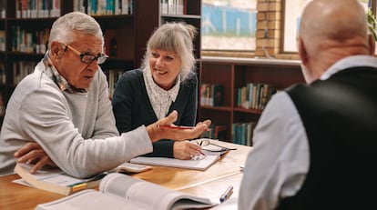 Un grupo de mayores se sienta para trabajar y debatir alrededor de una mesa en una biblioteca pública.