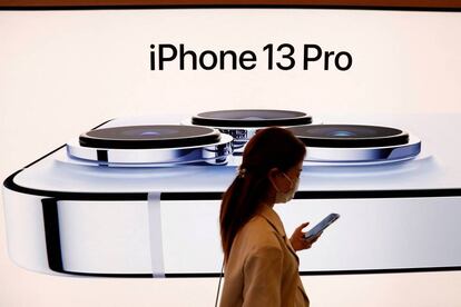 FILE PHOTO: A woman wearing a face mask walks past an image of an iPhone 13 Pro at an Apple Store in Beijing