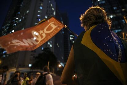 Manifestante enrolada na bandeira do Brasil olha para a bandeira de Dilma Rousseff no Rio de Janeiro.