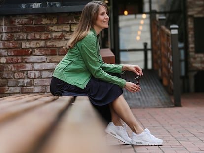 Una mujer sentada en un banco en la calle con zapatillas blancas.