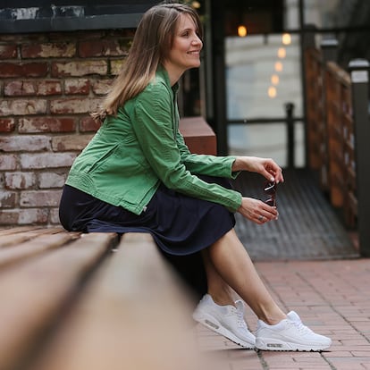 Una mujer sentada en un banco en la calle con zapatillas blancas.