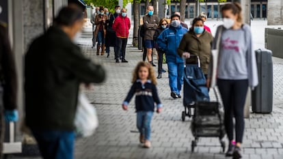 Una madre y su hija esperan en una cola para hacer la compra en Madrid, en una fila de personas protegidas con mascarillas frente al coronavirus.