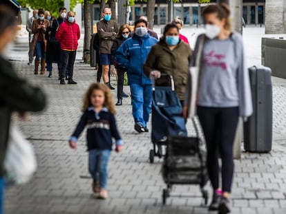 Una madre y su hija esperan en una cola para hacer la compra en Madrid, en una fila de personas protegidas con mascarillas frente al coronavirus.