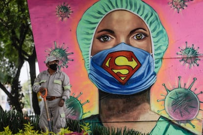 Un jardinero trabaja junto a un mural que muestra a una trabajadora sanitaria con una mascarilla, firmada por el artista urbano Applez, en la Ciudad de México.