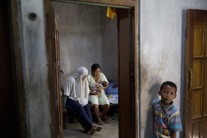 Nanai, trabajadora de salud comunitaria voluntaria, conversa con Sujilah, quien está amamantando a su bebé de cinco días en una habitación de la casa de la familia, en el pueblo de Dukuh (Indonesia). Un muchacho joven está por el umbral. Nanai trabaja por las mañanas y por las tardes es voluntaria, y asesora a las mujeres de la comunidad en cuestiones de salud. "Muchas vienen a mí para obtener información. Quieren saber cómo preparar los alimentos para su bebé y su familia y cuándo deben comenzar a dar sólidos a su hijo", dice.