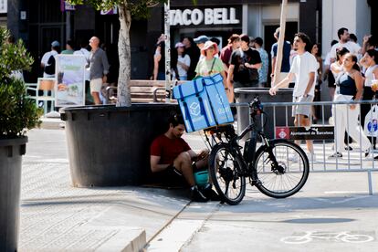 Un 'rider' se protege del calor durante un descanso, a la sombra de un árbol en Barcelona.