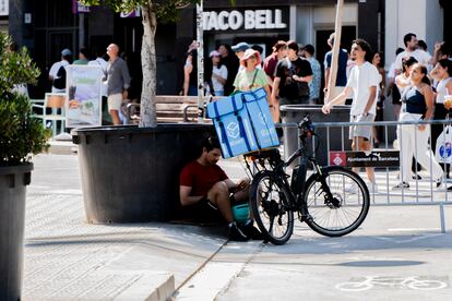 Un 'rider' se protege del calor durante un descanso, a la sombra de un árbol en Barcelona.
