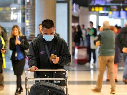 Un viajero, recién llegados al aeropuerto de Manises, consulta su móvil protegido con una mascarilla. 