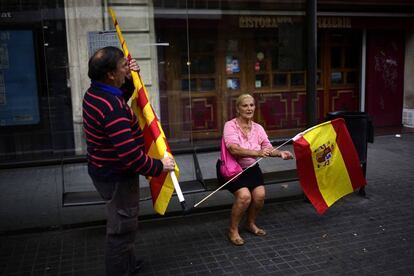 Una pareja espera el autobús con banderas de España y Cataluña, en Barcelona.