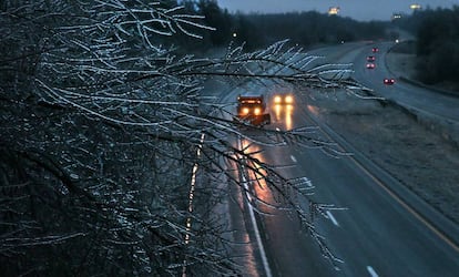 Una rama de árbol congelada por las bajas temperaturas, en primer plano, mientras un camión extiende sal en una carretera interestatal en Festus (Illinois).