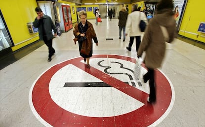 Dos personas pasan sobre una enorme se&ntilde;al de prohibido fumar en el Metro de Madrid, en 2005.