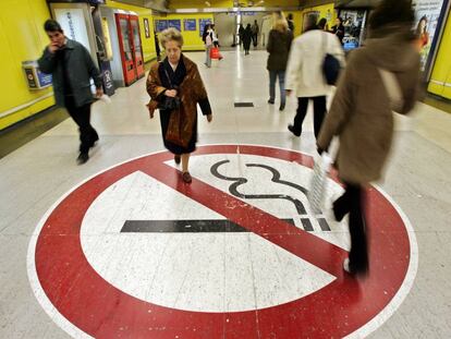 Dos personas pasan sobre una enorme se&ntilde;al de prohibido fumar en el Metro de Madrid, en 2005.