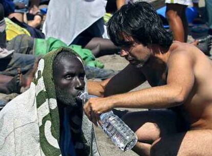 Un bañista da de beber a un inmigrante extenuado, en la playa de la Tejita, en Granadilla (Tenerife), el 30 de julio de 2006.