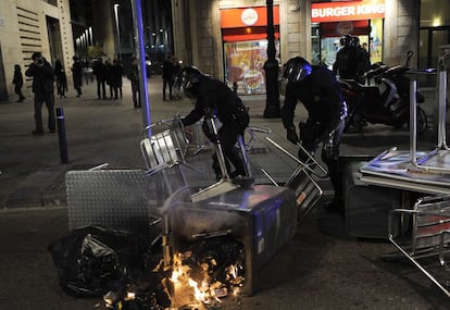 Un grupo de policías retiran de las calles mesas y sillas esparcidas en medio de una calle del centro de Bracelona mientras arde la basura de un contenedor.