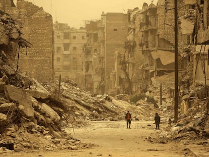 Dos sirios caminan entre los escombros durante una tormenta de arena en el barrio de Kastal al-Harami, en Alepo (Siria).