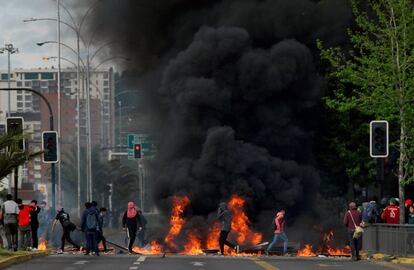 Los manifestantes se paran junto a una barricada en llamas, levantada en protesta por el aumento del precio del transporte público, este domingo, en Santiago de Chile. Los incendios se han replicado en estaciones de metro, autobuses, monumentos públicos, bancos, supermercados y universidades.